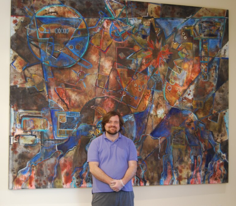 Jason Stallings standing in front of a large scale art commission after it's built and hung on site in the client's front entry way